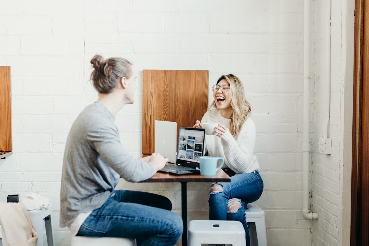 カフェの小さなテーブルでノートPCとコーヒーを挟んで向き合って話す2人