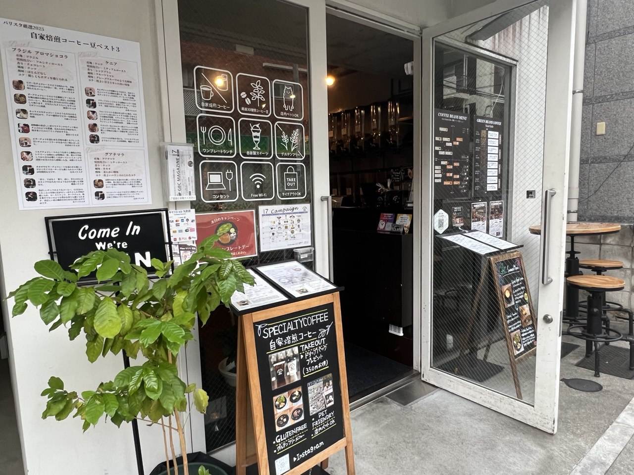 観葉植物とCome Inの黒板が置かれた看板のないグリーンビーンズコーヒーの入り口