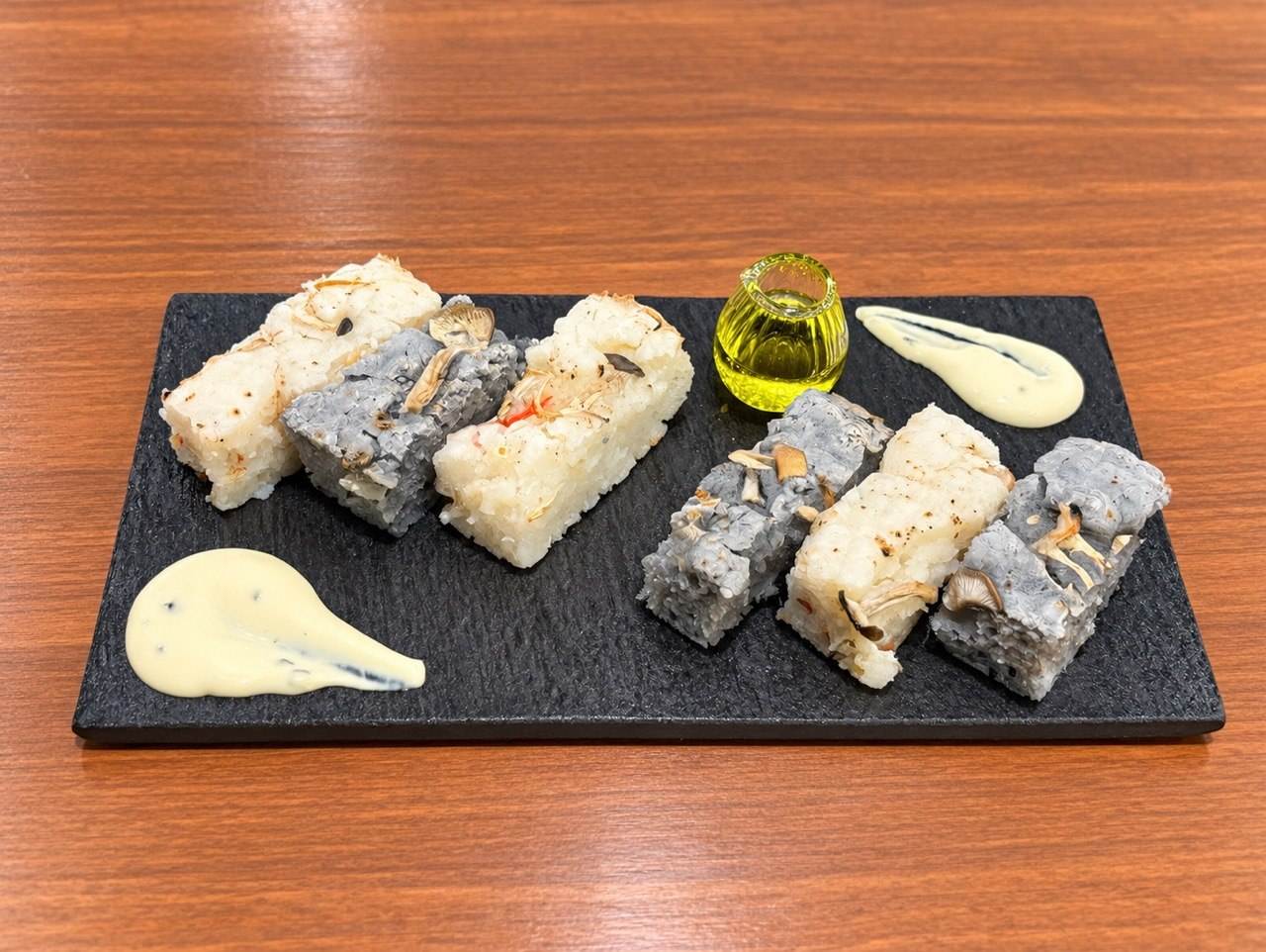 黒い石のプレートに並んだ白と竹炭色の米粉フォカッチャ、オイルとディップソースが添えられている